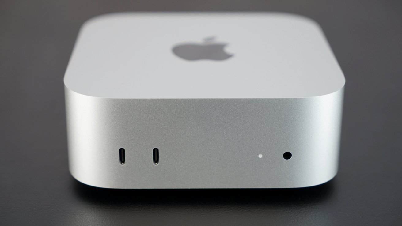 Silver-colored computer device with a sleek, minimalist design, featuring the Apple logo on top, two USB-C ports, a small hole, and a power indicator on the front.