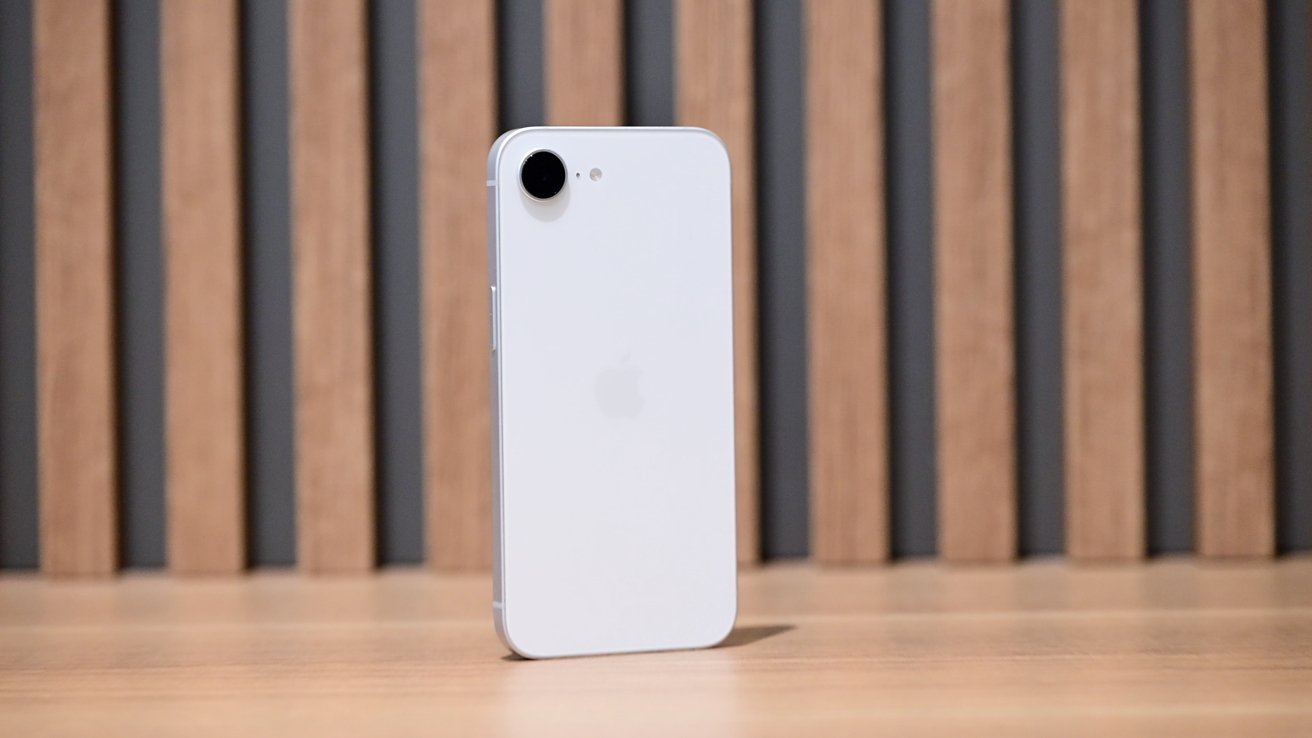 A white smartphone with a single camera on a wooden surface, vertical wooden slats in the background.