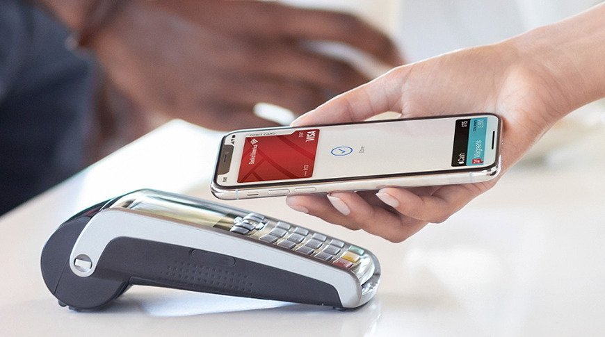 A person holds a smartphone near a contactless payment terminal, displaying a digital wallet app ready for transaction.